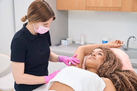 Dermatologist doctor consulting a young woman on the problem of hyperhidrosis in a modern clinic of aesthetic medicine